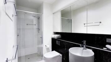 A modern bathroom with a glass-enclosed shower, a white toilet, and a black marble sink.