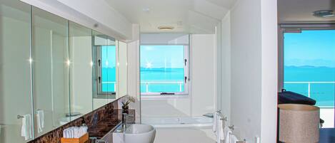 Ein modernes Badezimmer mit zwei Waschbecken, einer Badewanne und einem großen Spiegel. Durch ein Fenster ist Meerblick.