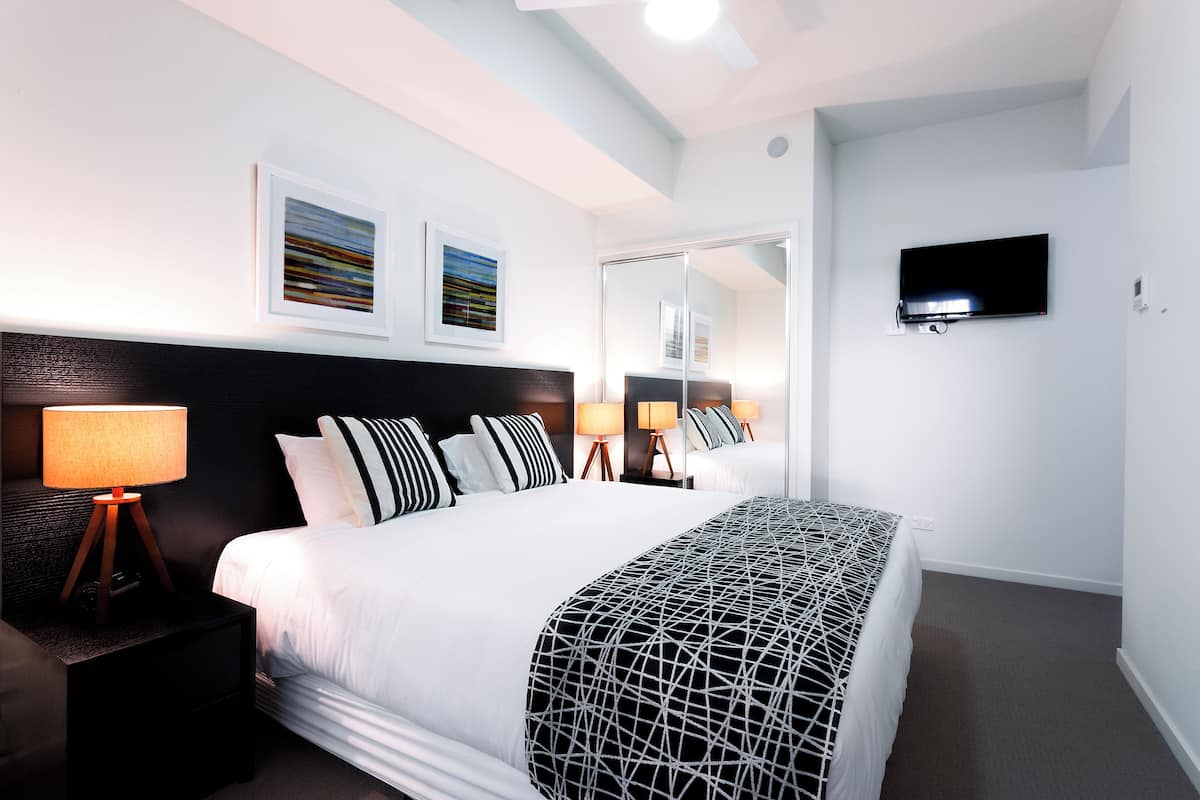 Ein modernes Hotelzimmer mit einem großen Bett, Nachttischlampen, einem Flachbildfernseher und Kunstwerken an den Wänden.