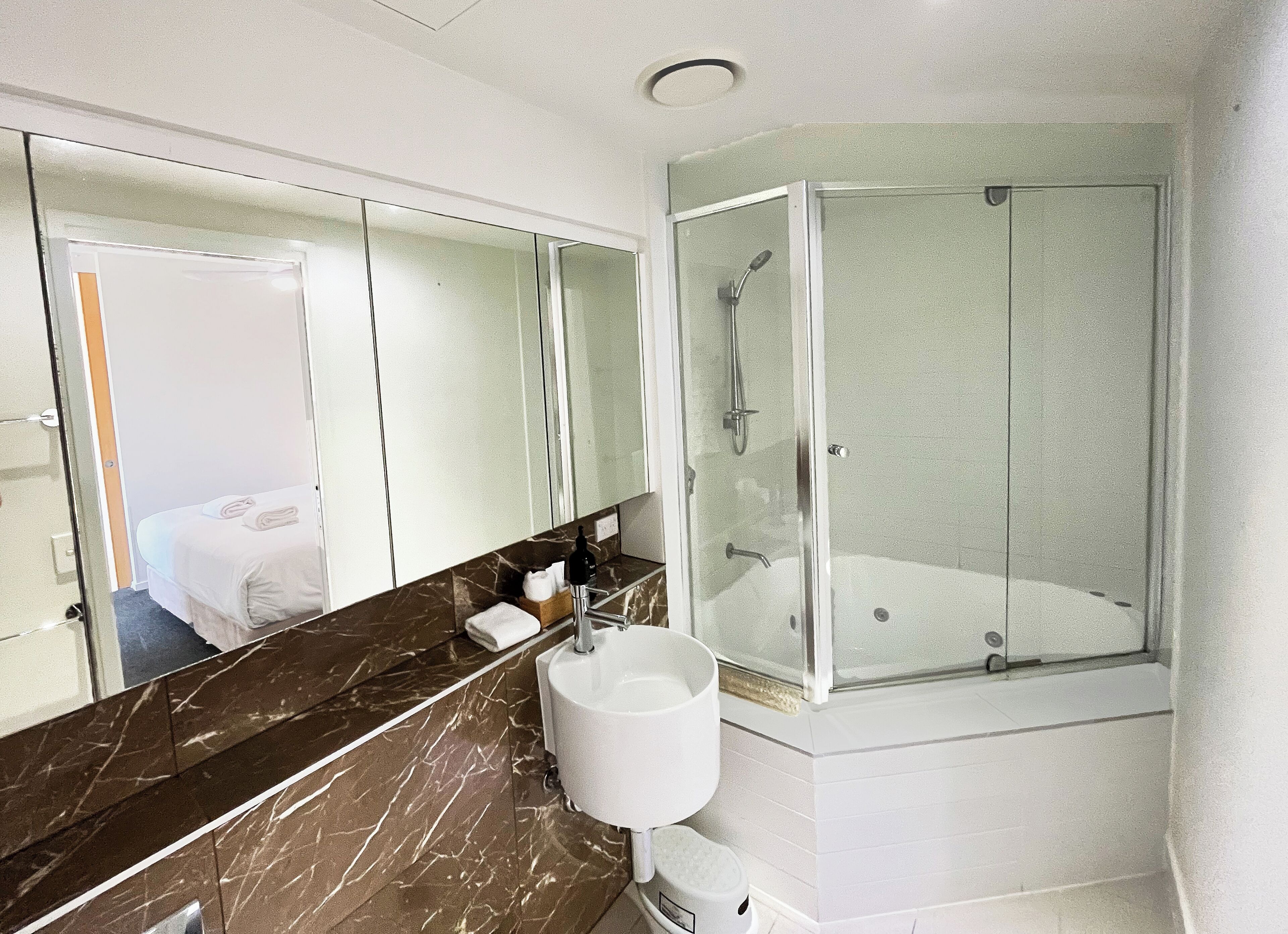 Un baño moderno con encimera de mármol, un espejo grande, cabina de ducha y lavamanos.