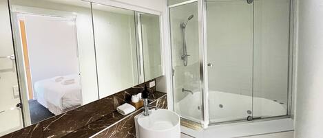 Un baño moderno con encimera de mármol, un espejo grande, cabina de ducha y lavamanos.