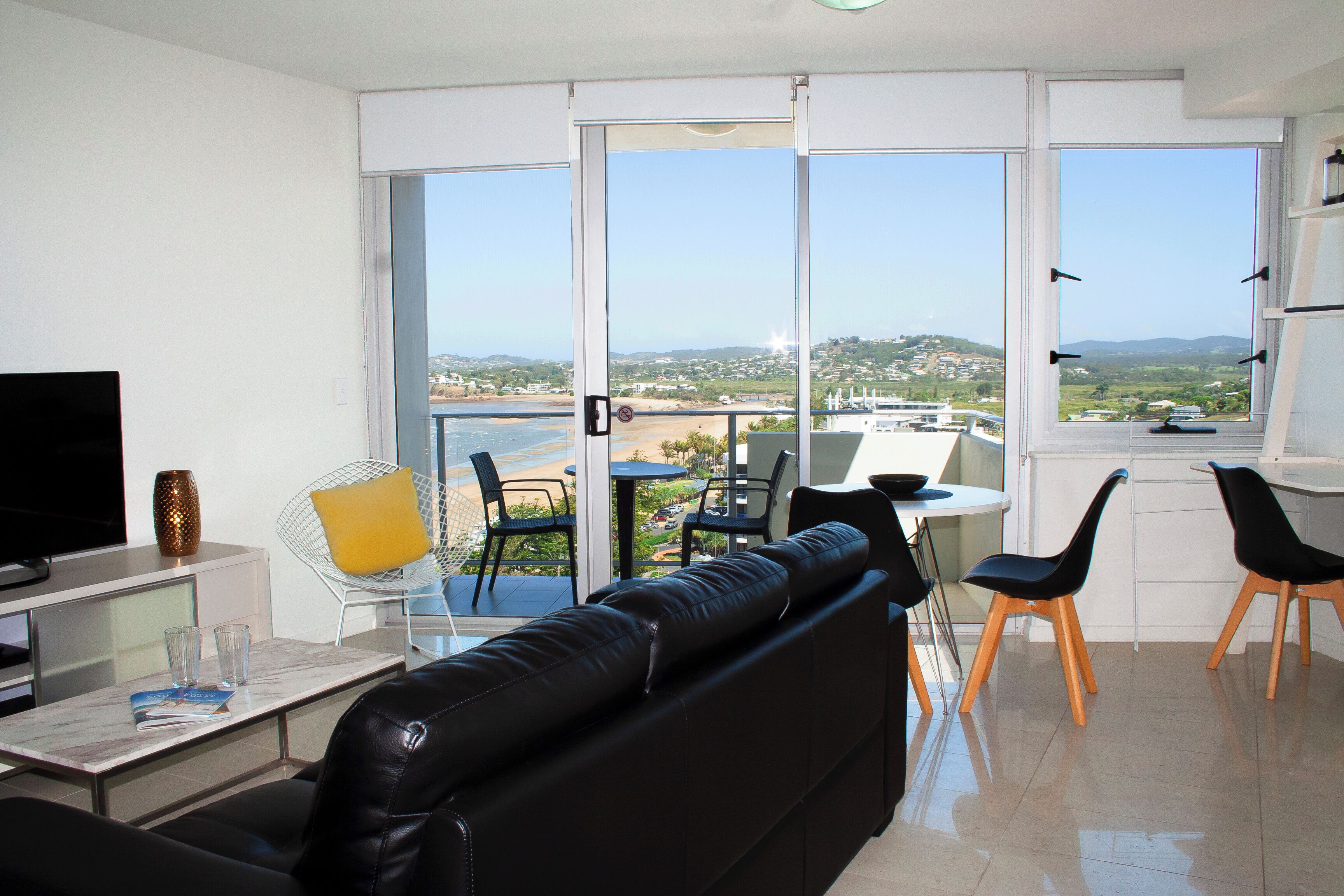 Una sala de estar moderna con un sofá de cuero negro, un televisor de pantalla plana y un comedor con sillas y una mesa.