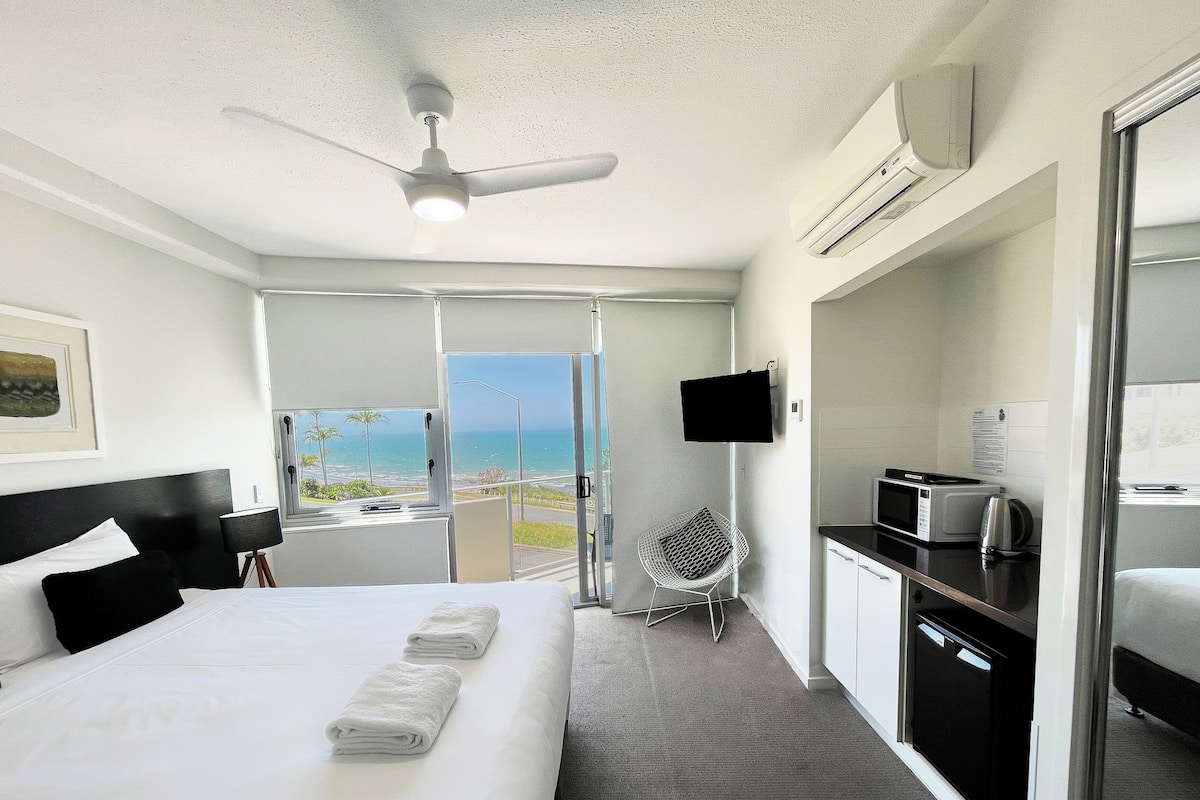 Ein Hotelzimmer mit Bett, Schreibtisch mit Mikrowelle, Stuhl, Fernseher und Meerblick.