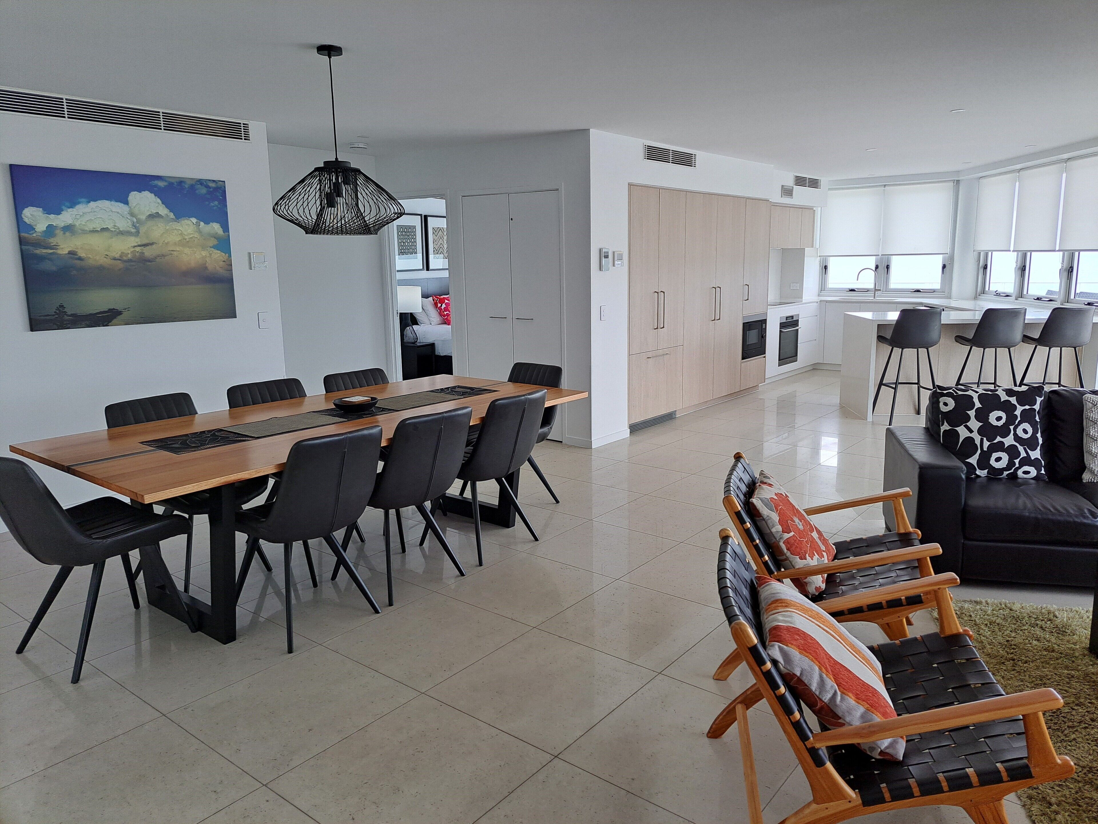 A modern living room with a dining area, a kitchen, and a view of the outside.