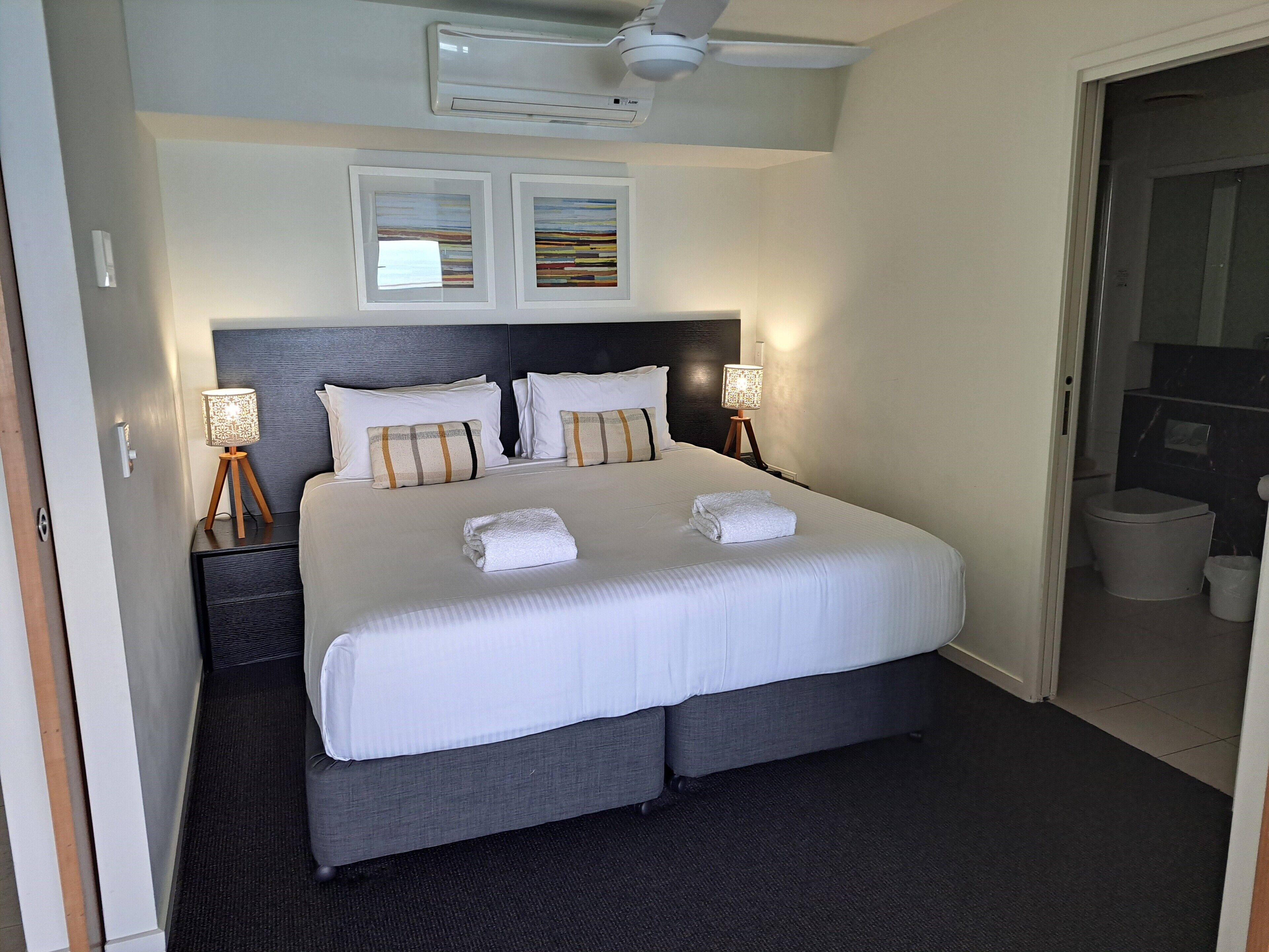 A neatly made bed with white linens and two pillows, a bedside lamp, and a ceiling fan in a hotel room.