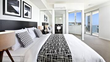 Una habitación de hotel moderna con una cama grande, un balcón con vistas a la ciudad y un baño con ducha e inodoro.