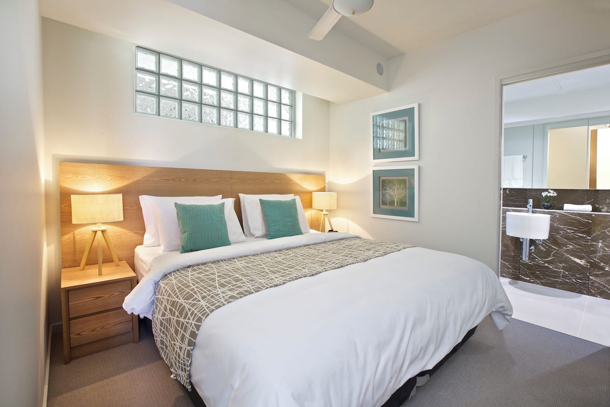 Ein Hotelzimmer mit einem großen Bett, zwei Nachttischen mit Lampen, einem Deckenventilator, einem Fenster mit Aussicht und einem Badezimmer mit Marmorwaschbecken.