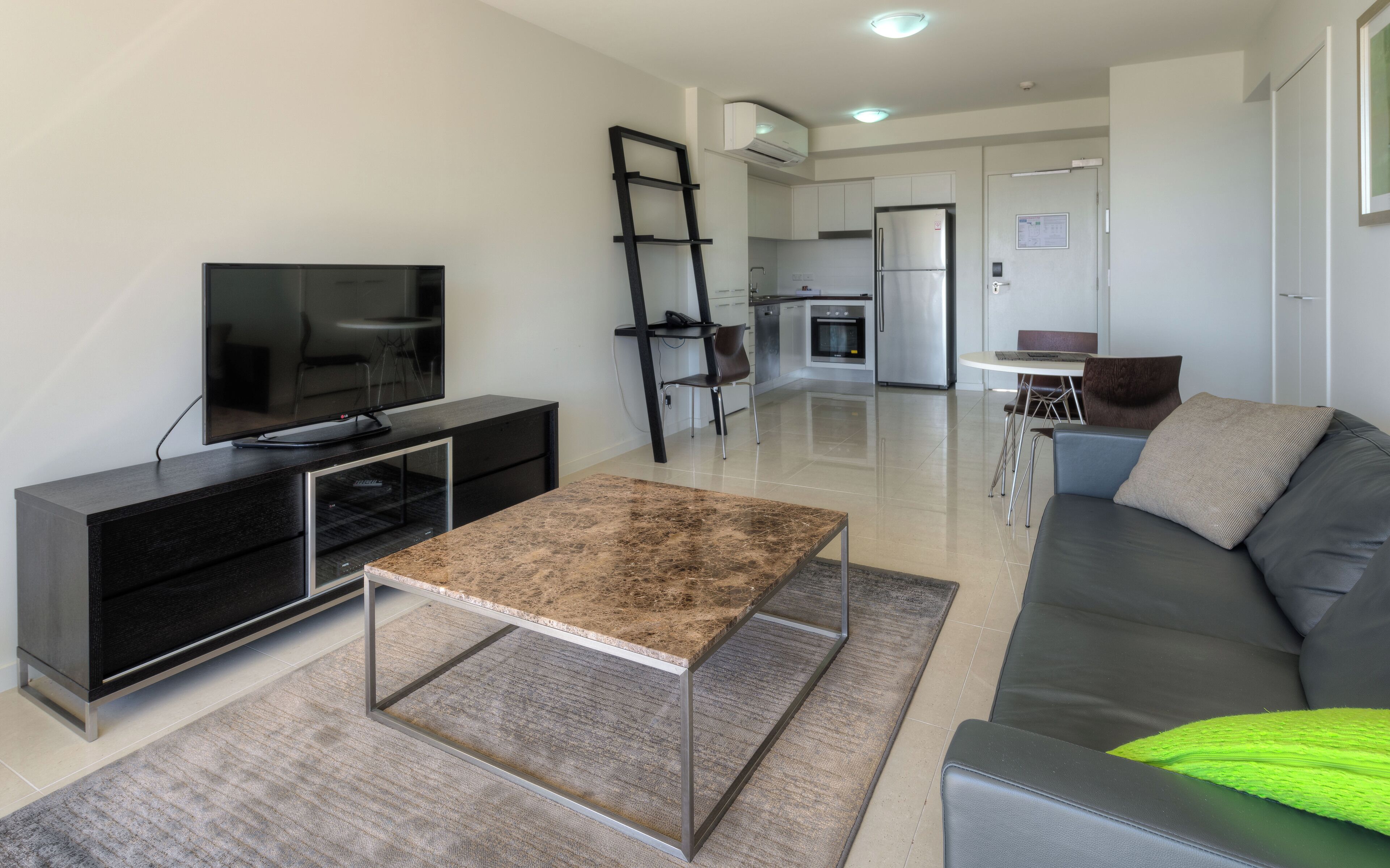 Una sala de estar moderna con televisor de pantalla plana, una mesa de centro, un sofá y una cocina al fondo.