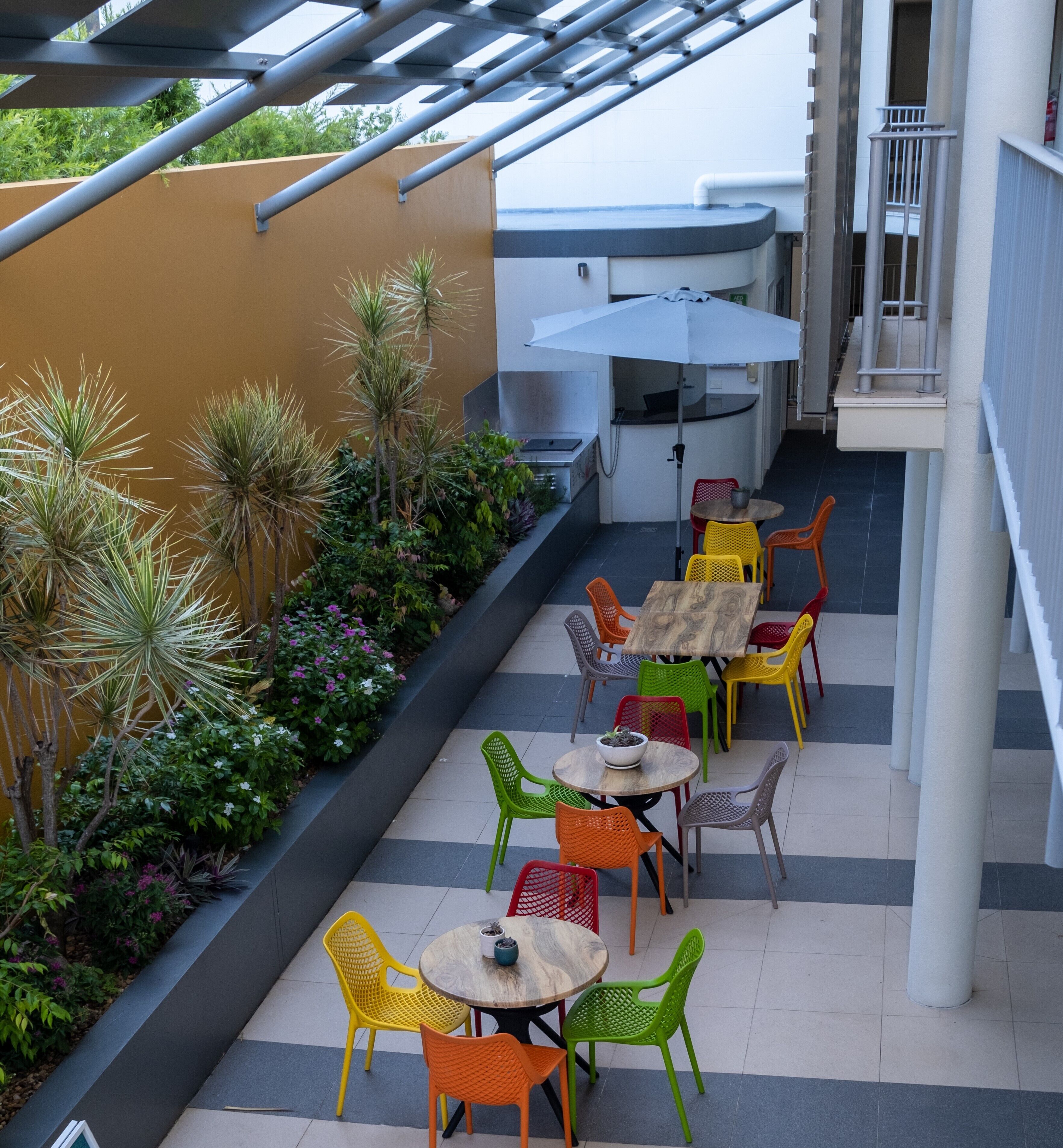 An outdoor patio area with multiple tables and chairs, surrounded by plants and a barbecue grill.
