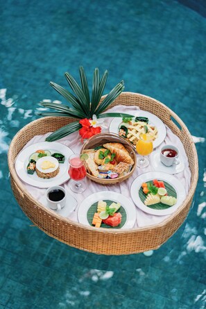 A floating dining setup with various food items and drinks on a poolside table. - The Bali Dream Suite Villa Seminyak (Seminyak)
