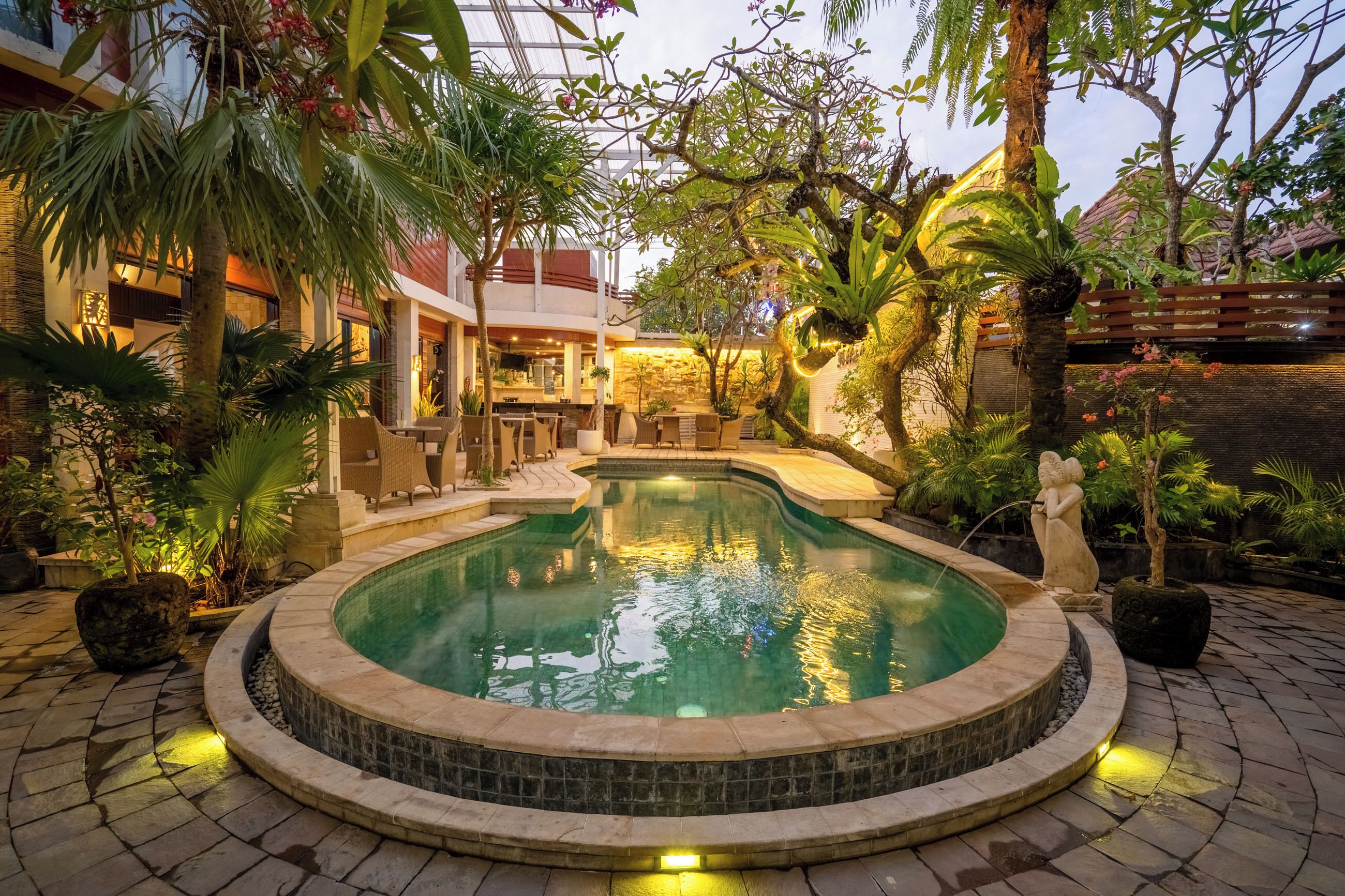 An indoor pool area with a stone edge, surrounded by tropical plants and a wooden deck.