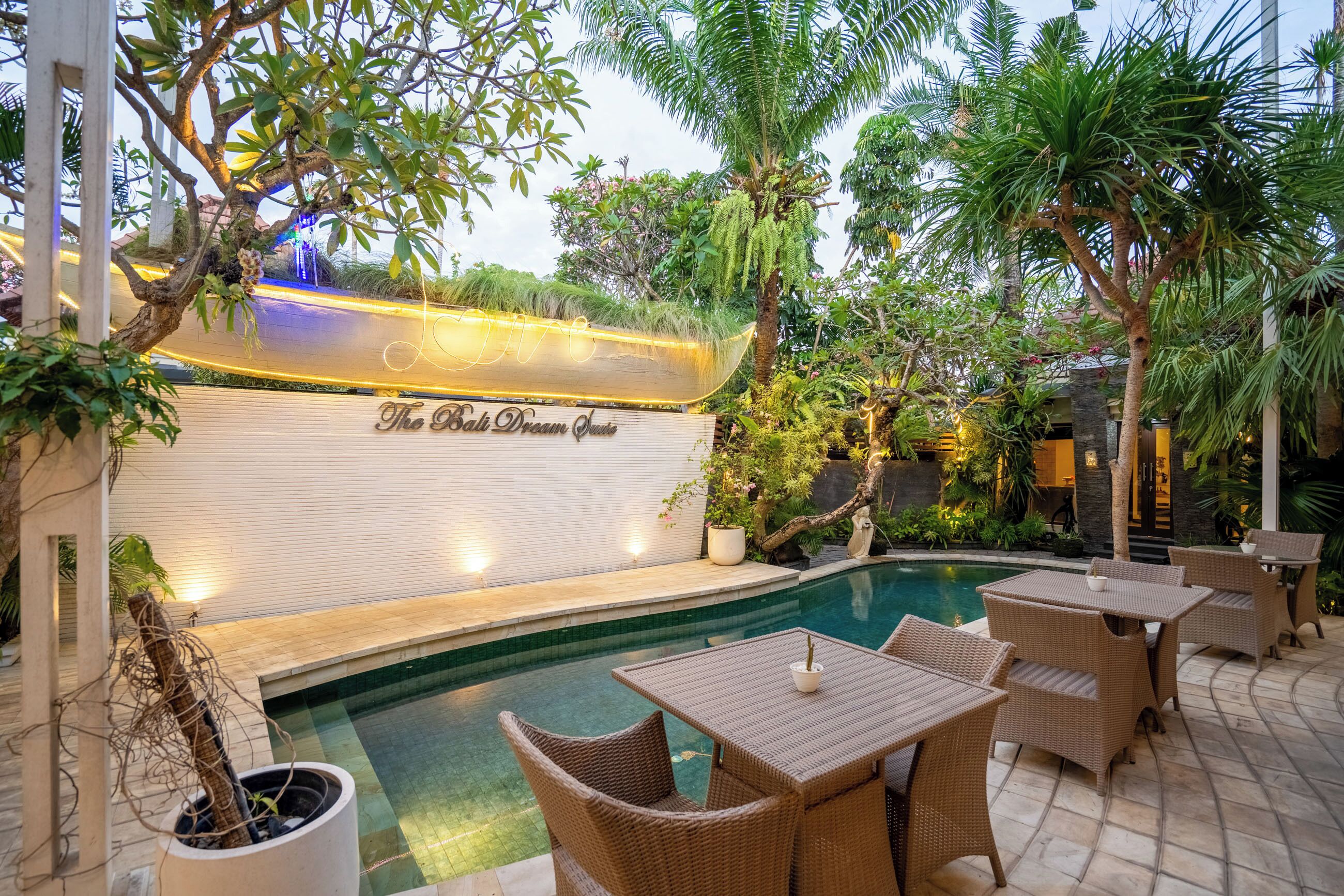 A poolside area with wicker furniture, a wall with a sign, and lush greenery.