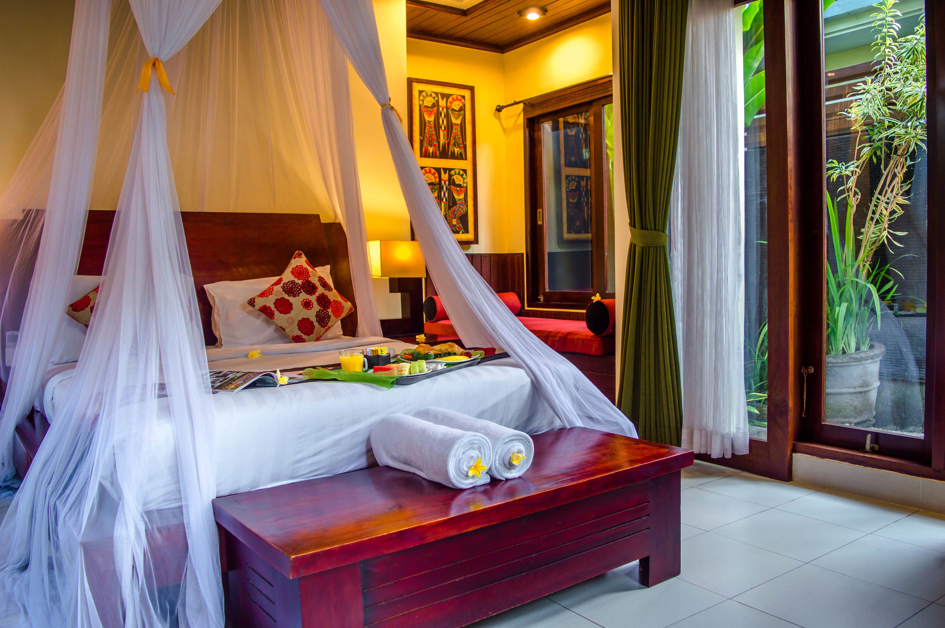 A four-poster bed with a canopy, a bedside table, and a bench with towels.