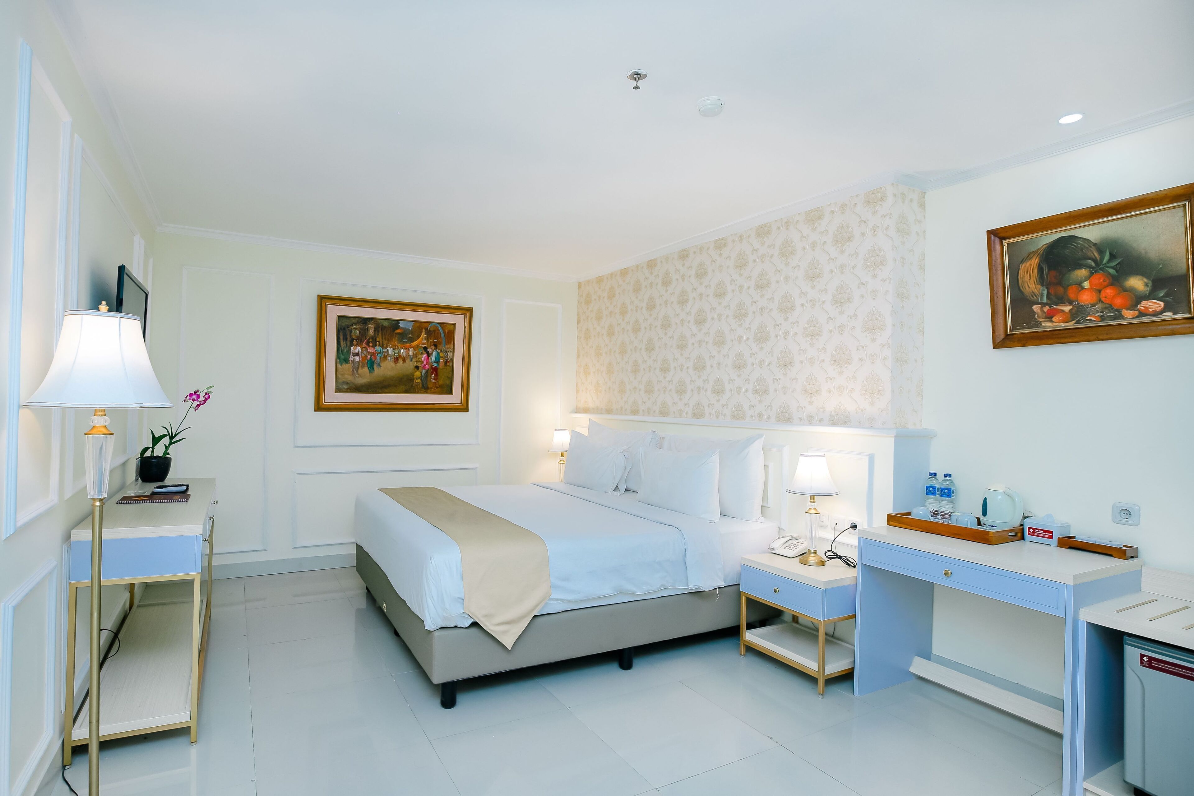 A hotel room with a bed, bedside tables, a desk, and a painting.