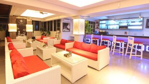 A modern lounge area with white sofas and red cushions, a bar with illuminated screens, and a clean, bright interior. - The Cube Malioboro Hotel (Yogyakarta)