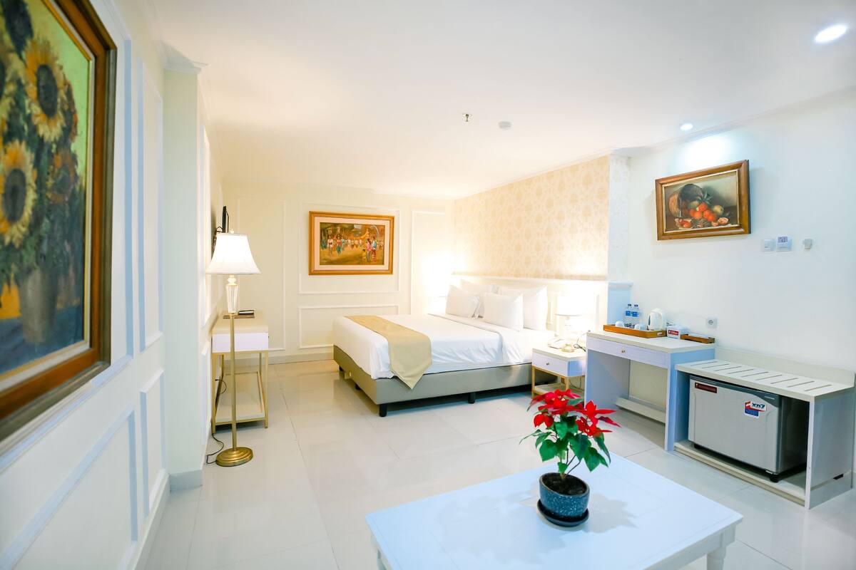 A hotel room with a bed, bedside table, lamp, and a small kitchenette area.
