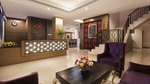A hotel lobby with a reception desk, a staircase, and purple seating. - The Cube Malioboro Hotel (Yogyakarta)