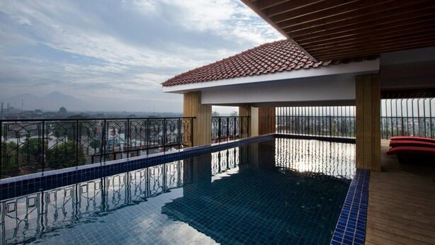 A rooftop infinity pool with a wooden deck, metal railing, and a view of the cityscape. - The Cube Malioboro Hotel (Yogyakarta)