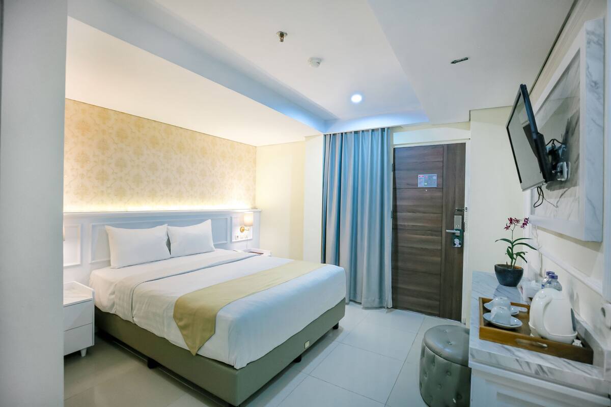 A modern hotel room with a large bed, a bedside table, a TV mounted on the wall, and a bathroom with a toilet and sink.
