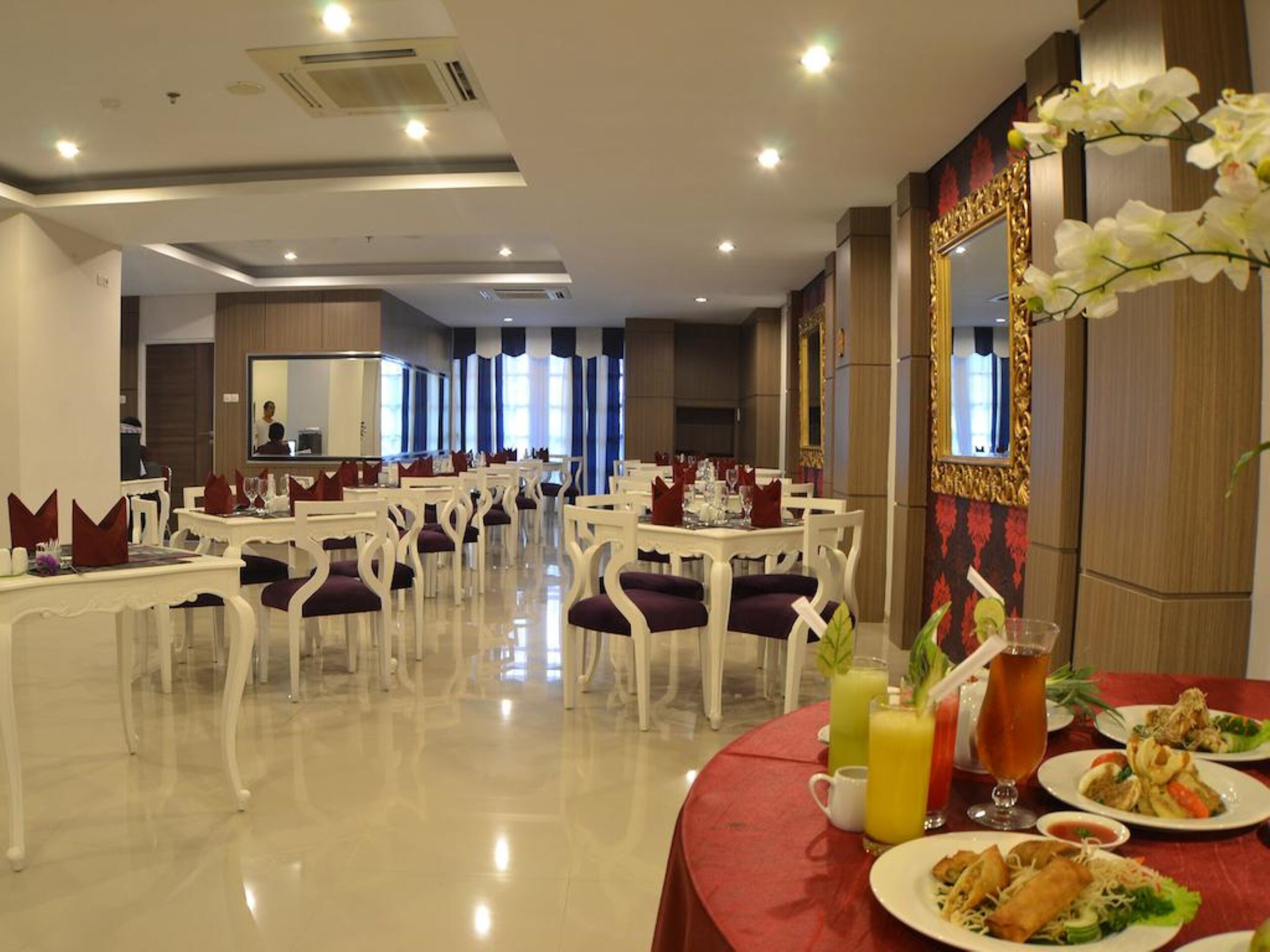 Un comedor de hotel con varias mesas y sillas, suelo pulido y un espejo con marco ornamentado.