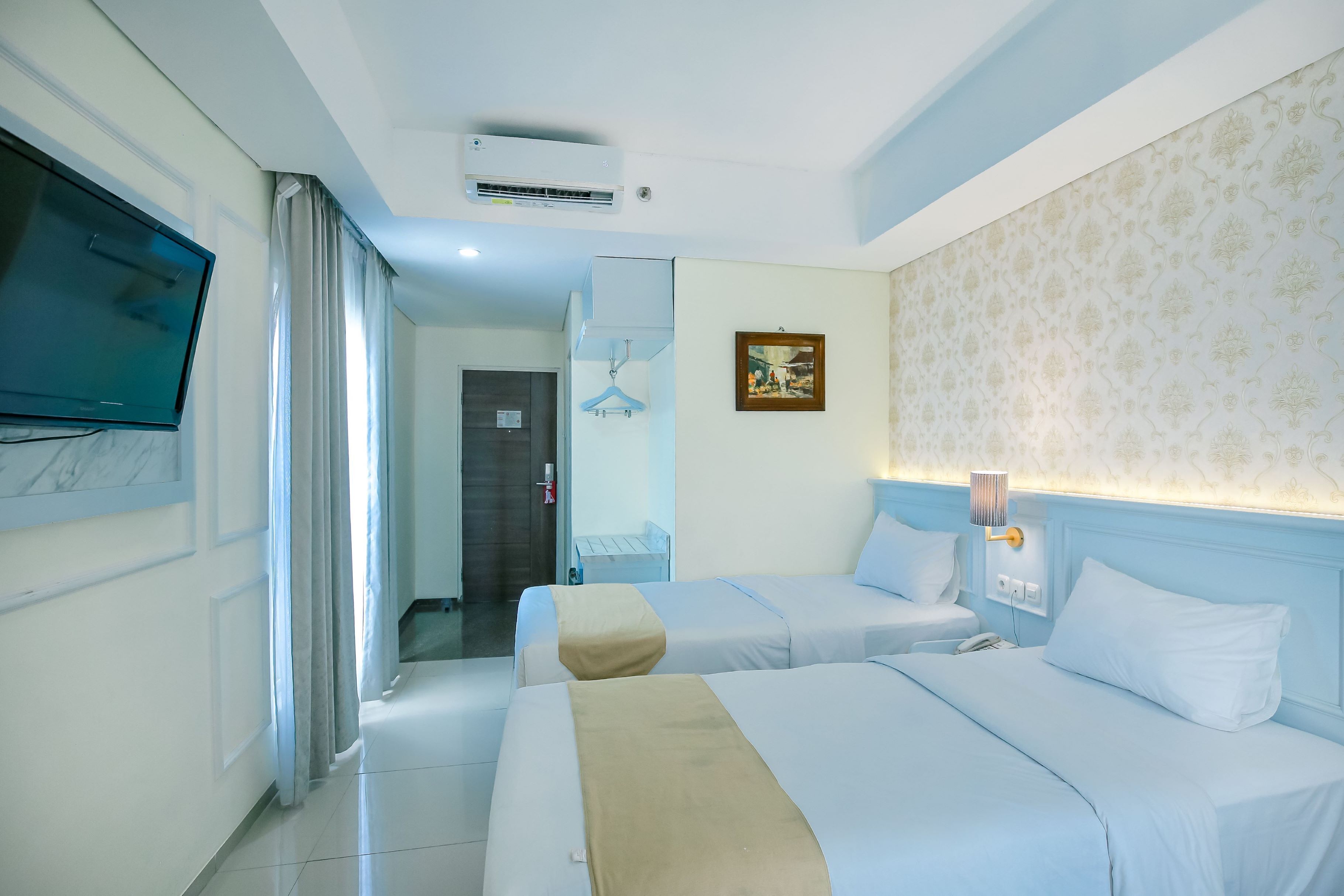 Una habitación de hotel con dos camas, televisión, un cuadro y pared con estampado.