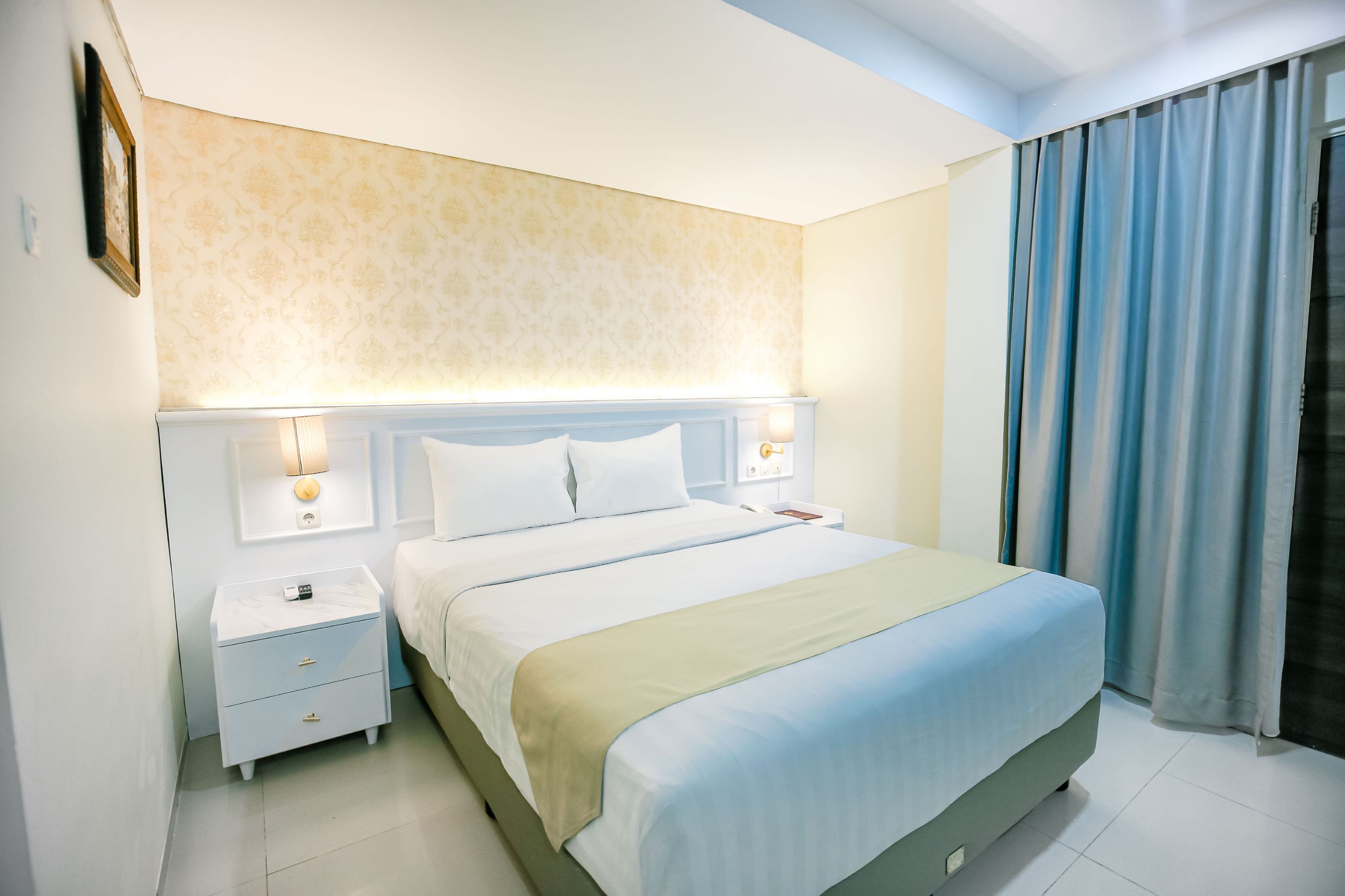 A modern hotel room with a large bed, bedside tables, and a nightstand.