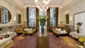 A hotel lobby with a central round table, multiple seating areas, and large windows. - LA Maison Hotel (Saarlouis)