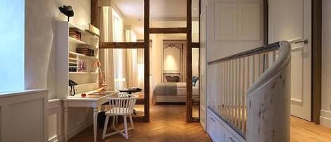 Un pasillo con suelo de madera, un escritorio blanco con una silla, una cama y una escalera con barandilla blanca.