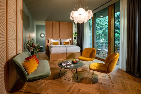 A modern hotel room with a large bed, a sofa, two armchairs, a round coffee table, and a balcony with a view of greenery. - LA Maison Hotel (Saarlouis)