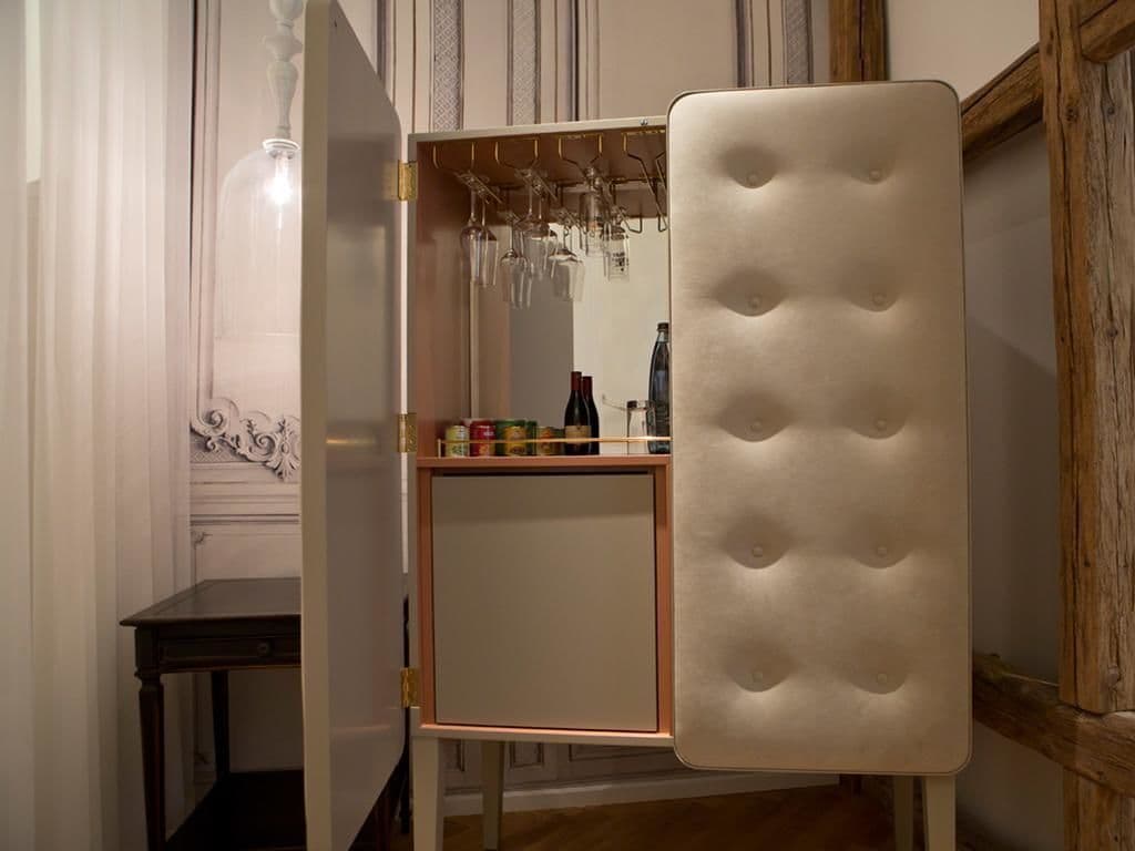 A compact minibar with a cushioned door, a wine glass holder, and a small shelf with bottles and cans.