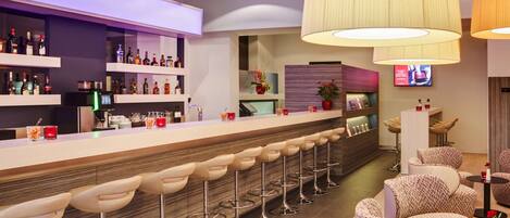 A modern bar area with a long counter, multiple stools, and a variety of bottles.