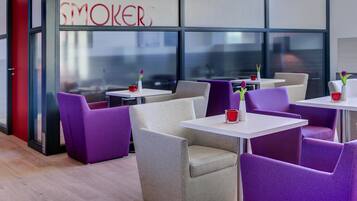 A modern indoor seating area with purple and beige chairs, white tables, and a glass wall with the word "SMOKERS" visible.