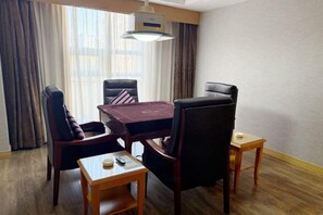 Une chambre d’hôtel avec un plancher en bois, une table à manger de couleur sombre et quatre chaises, une petite table d’appoint en bois et une grande fenêtre avec des rideaux.