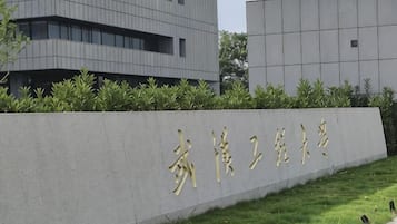 A building with a sign in gold characters, surrounded by a low hedge and grass.