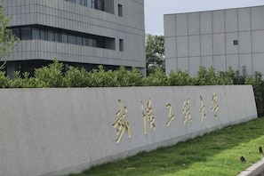 A building with a sign in gold characters, surrounded by a low hedge and grass.