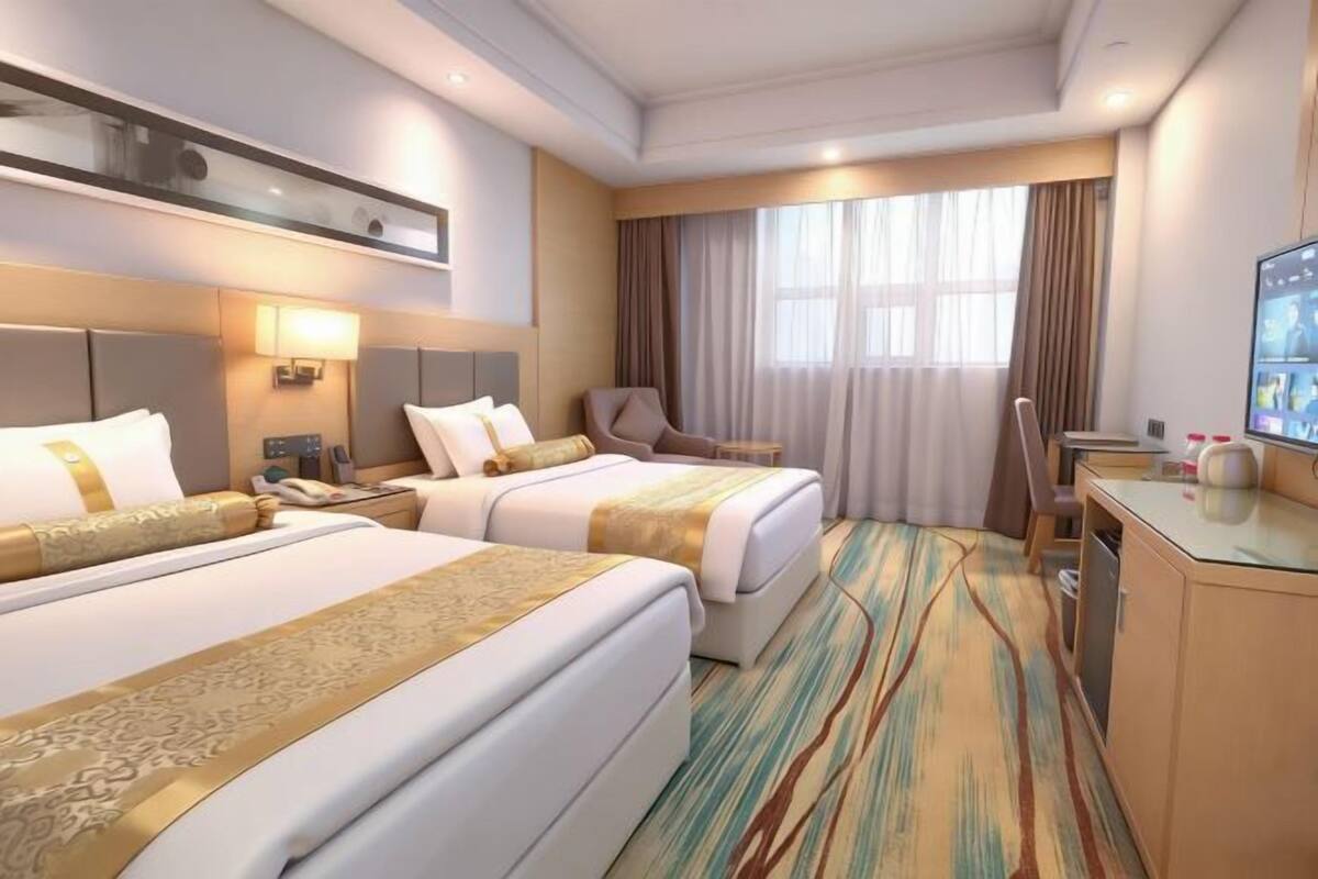 Ein Hotelzimmer mit zwei Betten, einem Schreibtisch, einem Sessel, einem Fernseher und einem Fenster mit Vorhängen.