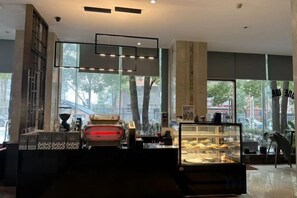 A modern interior with a reception desk, a display case with pastries, and large windows allowing natural light. - Xin A Dan Yuan Optics Valley International Hotel (Wuhan)