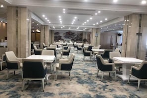 Un comedor de hotel con varias mesas y sillas, alfombra estampada y un diseño de techo moderno.
