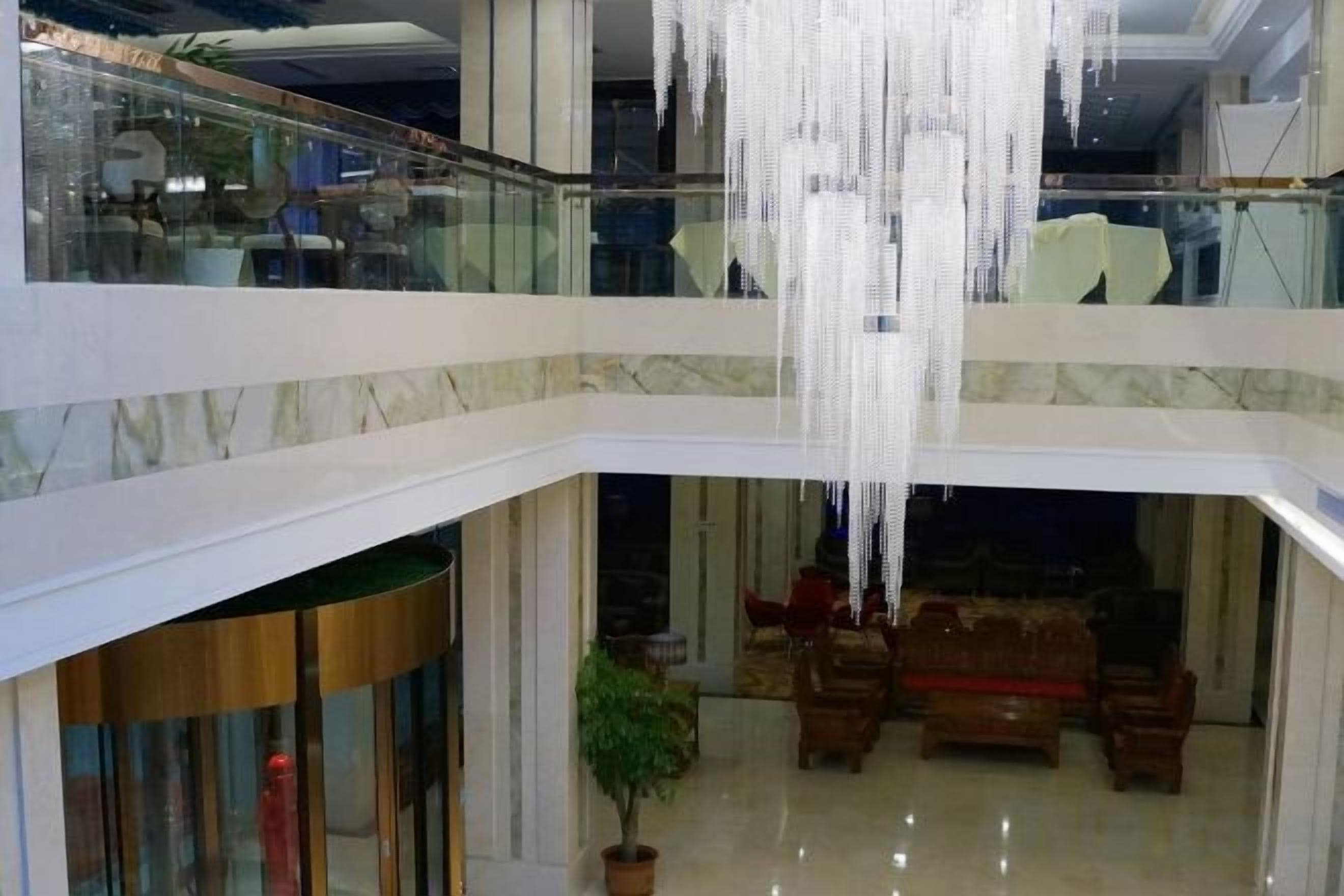 A multi-level atrium with a glass railing, a chandelier, and a seating area with sofas.