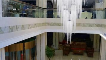 A multi-level atrium with a glass railing, a chandelier, and a seating area with sofas.
