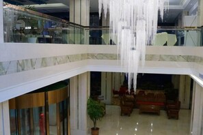 Un atrium à plusieurs niveaux, doté d’une balustrade en verre, d’un lustre et d’un espace détente avec des canapés.