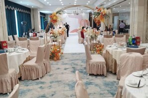 Une salle de banquet avec des tables rondes, des chaises et des centres de table floraux.