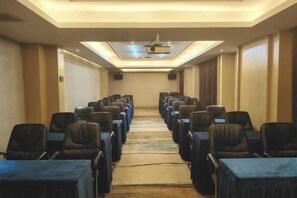 Une salle de conférence avec des rangées de chaises et de tables, un sol recouvert de moquette et un écran de projection à l’avant.