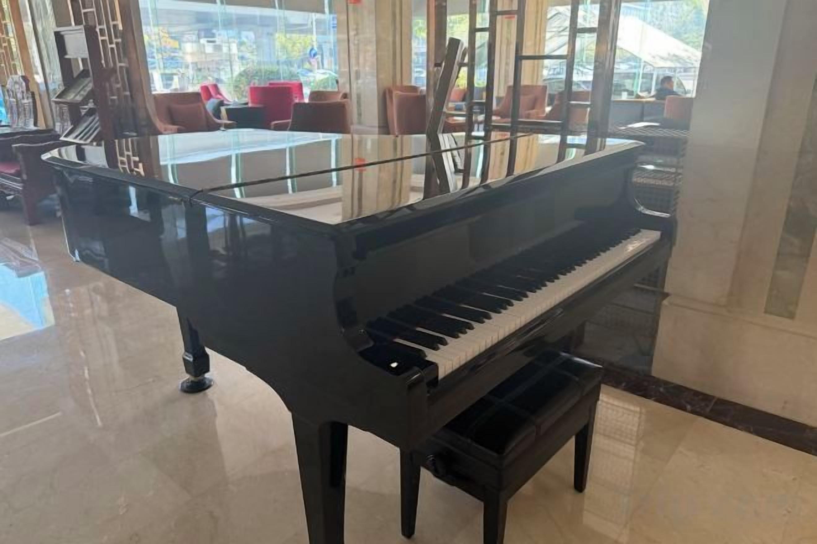 A grand piano in a spacious lobby with a glass partition, modern furniture, and a view of the outside.