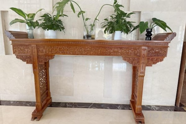 A wooden table with intricate carvings, flanked by potted plants.