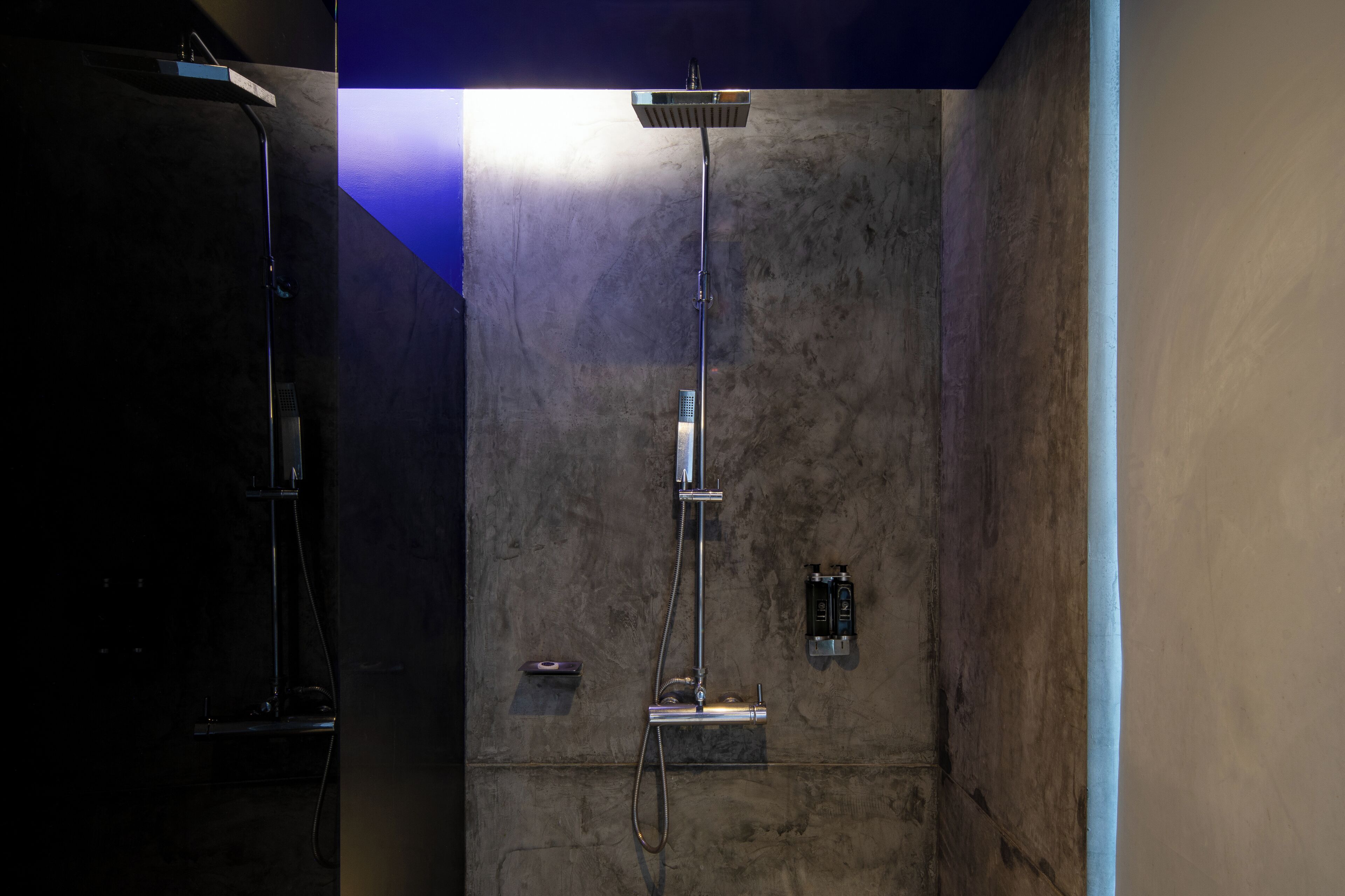 A modern shower area with a vertical rain showerhead and a handheld showerhead, set against a textured wall.