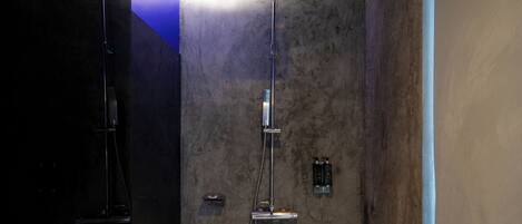 A modern shower area with a vertical rain showerhead and a handheld showerhead, set against a textured wall.
