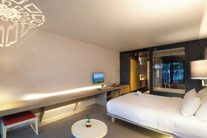 Una habitación de hotel moderna con cama, mesita de noche, televisor y una pequeña mesa redonda con una planta.