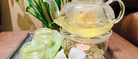 Une théière en verre avec un couvercle, deux tasses en verre et une fleur blanche sur un plateau.
