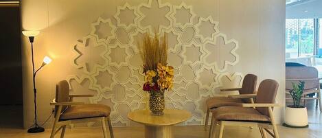 A modern lobby with a round table, two chairs, and a decorative wall with geometric patterns.
